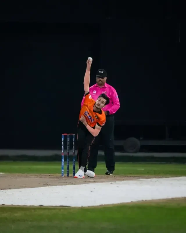 Bowler mid-delivery with an umpire looking on during a skills clinic