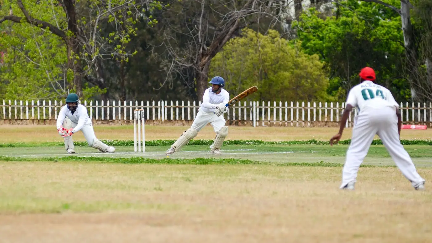 A cricket match in progress on a dry, worn subcontinent pitch