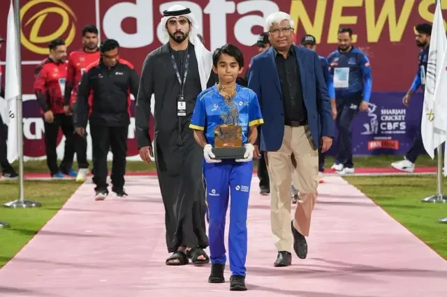 A young player being escorted to receive an award trophy on the pitch