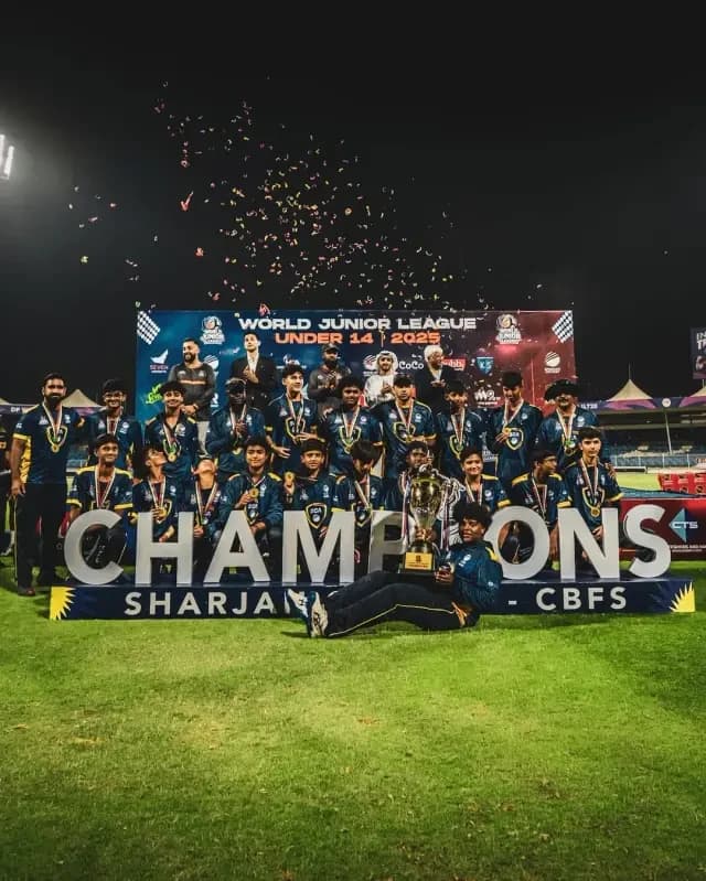 Youth cricket team celebrating with the champions trophy under stadium lights