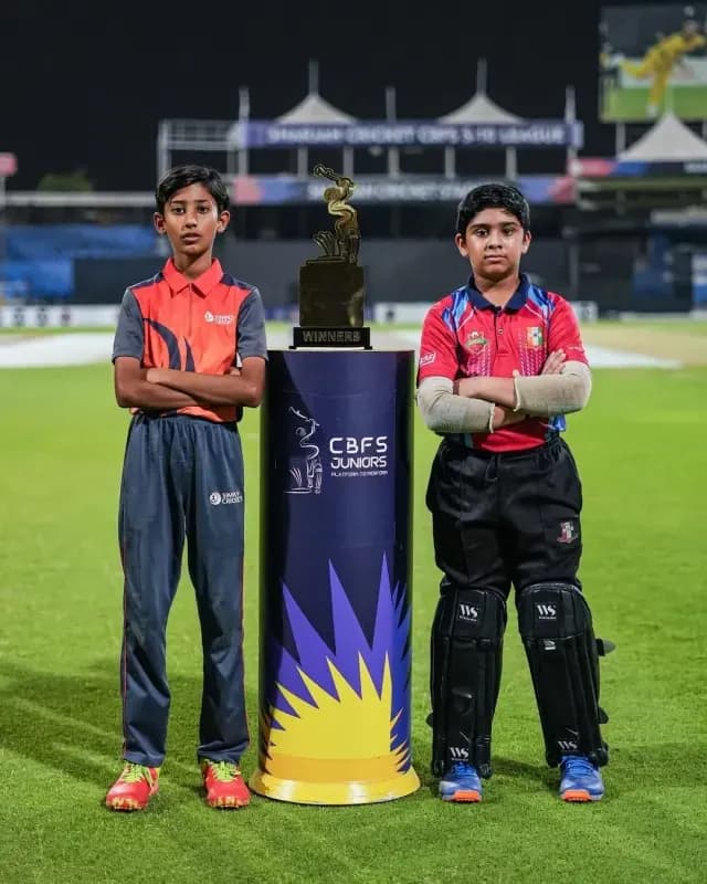 Two young cricketers in kit standing either side of the CBFS Juniors winners trophy