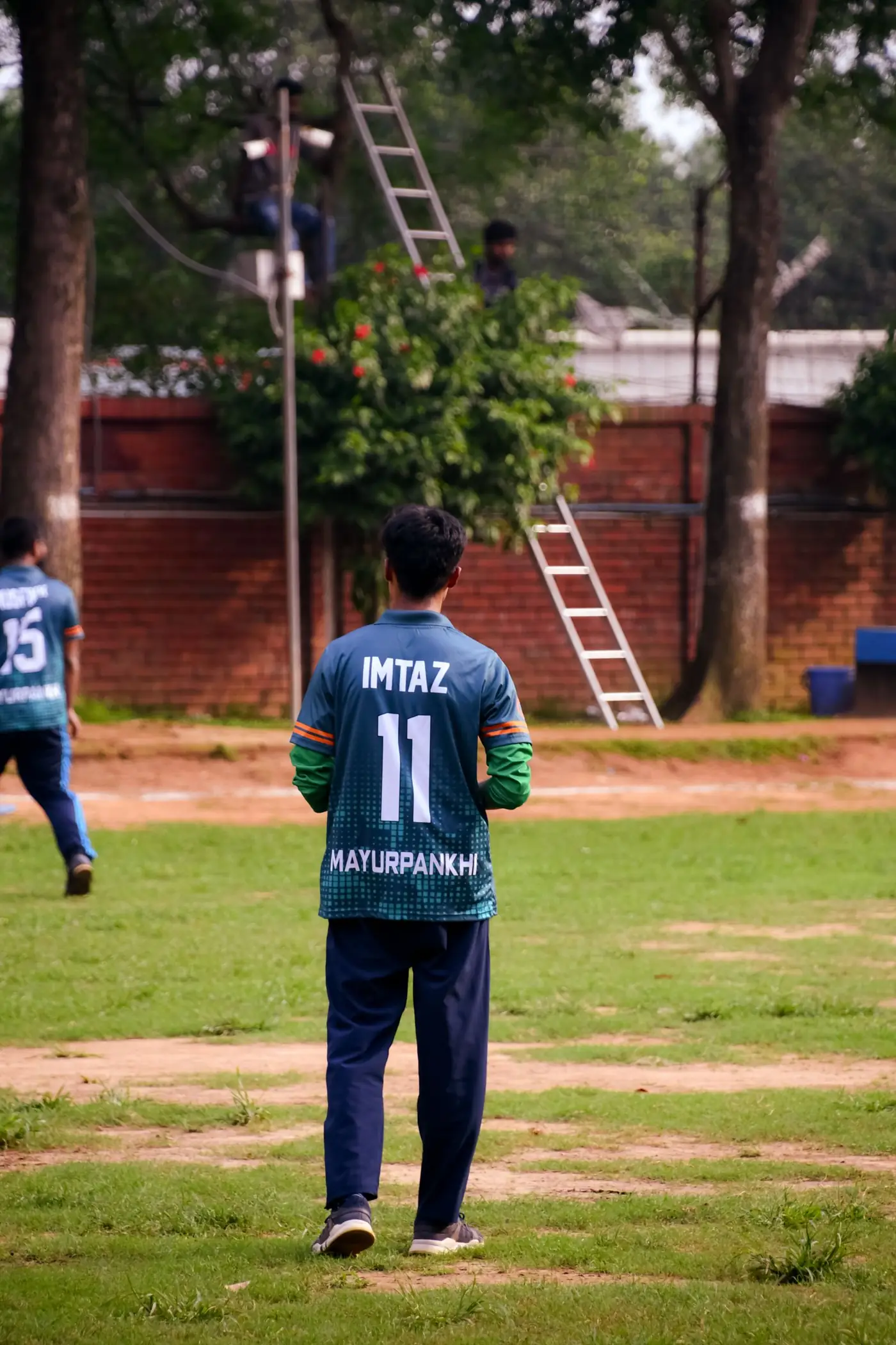 Young cricketer in team kit standing on the pitch with a teammate nearby