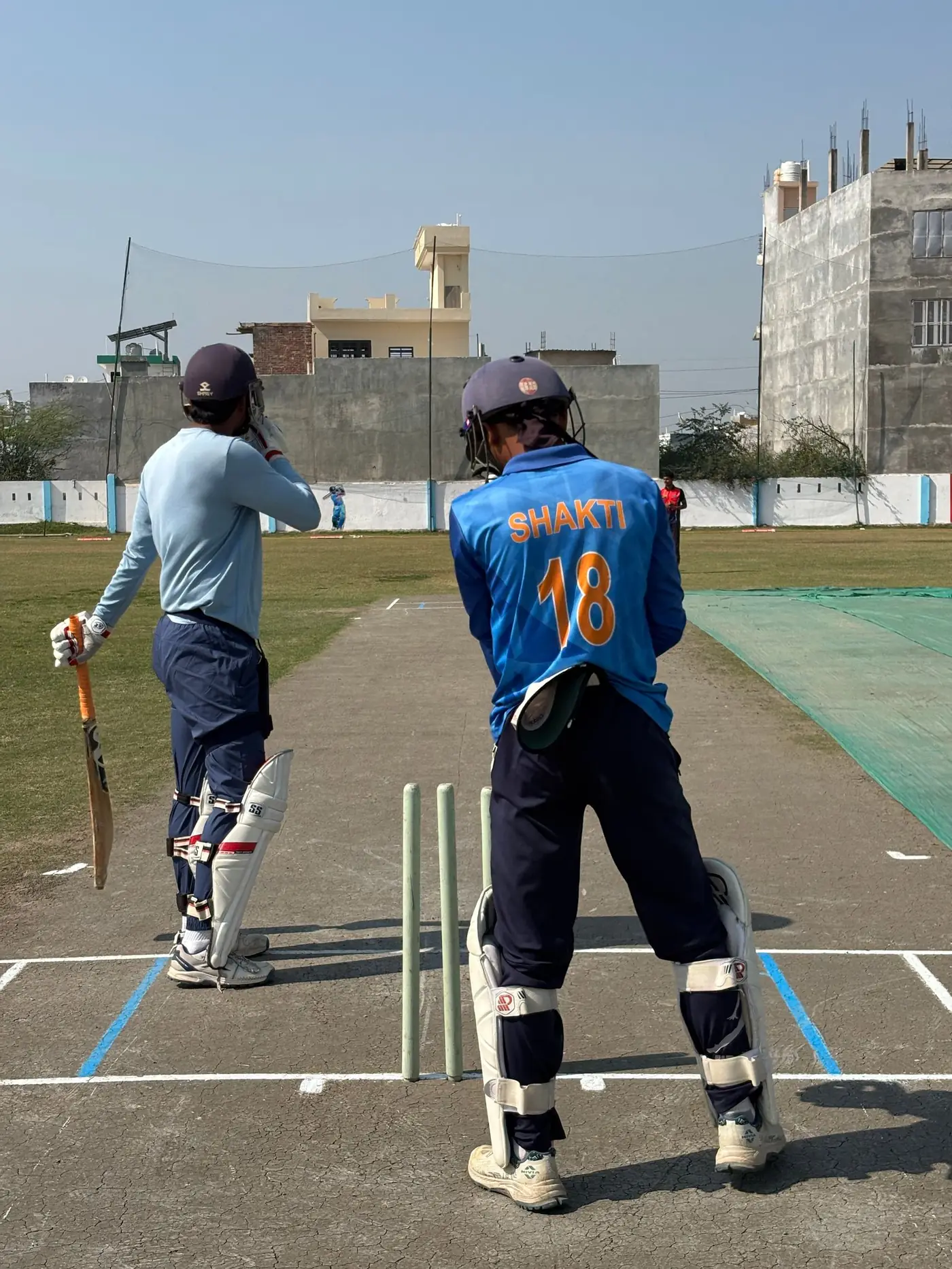 Two young batsmen in helmets and pads walking out together, bats in hand