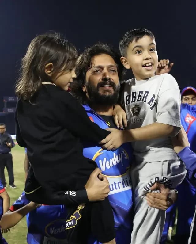 Bollywood actor carrying two children while greeting fans pitch-side