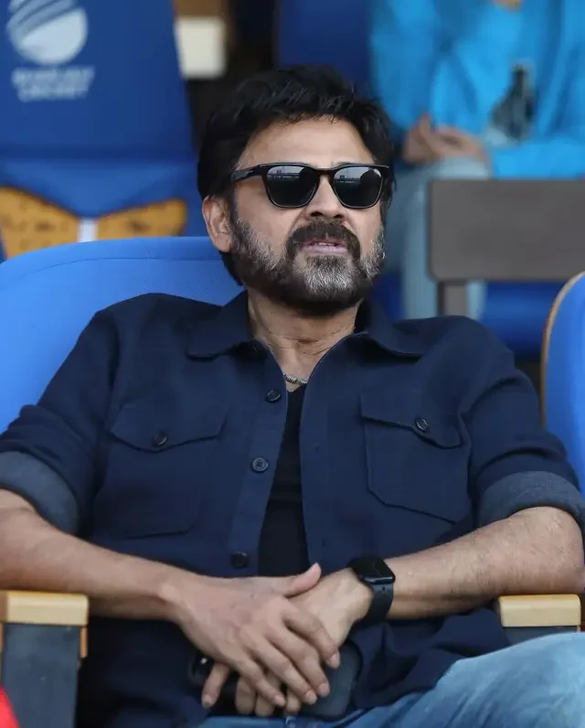 South Indian film actor seated pitch-side watching a match